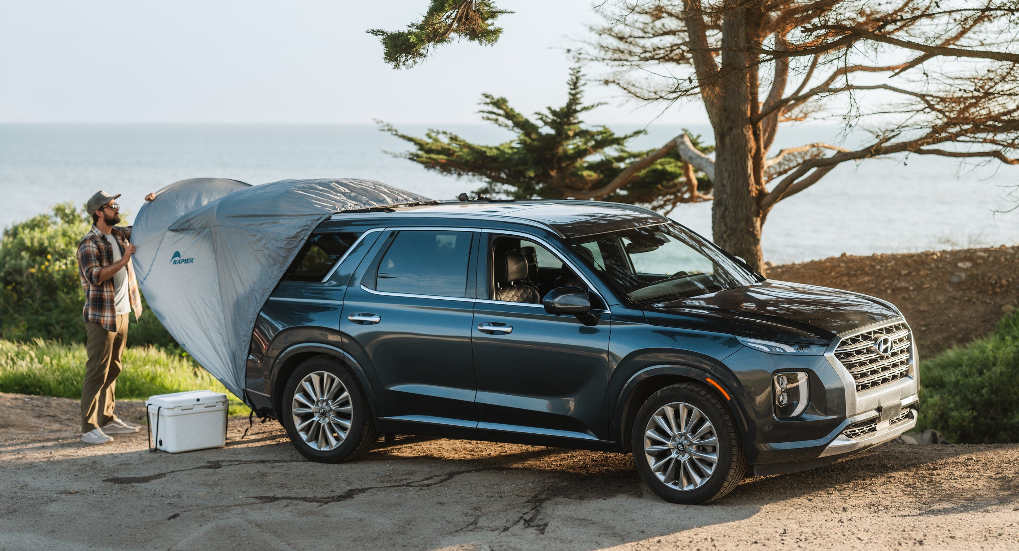 person setting up a sportz cove awning tent on a car next to the lake